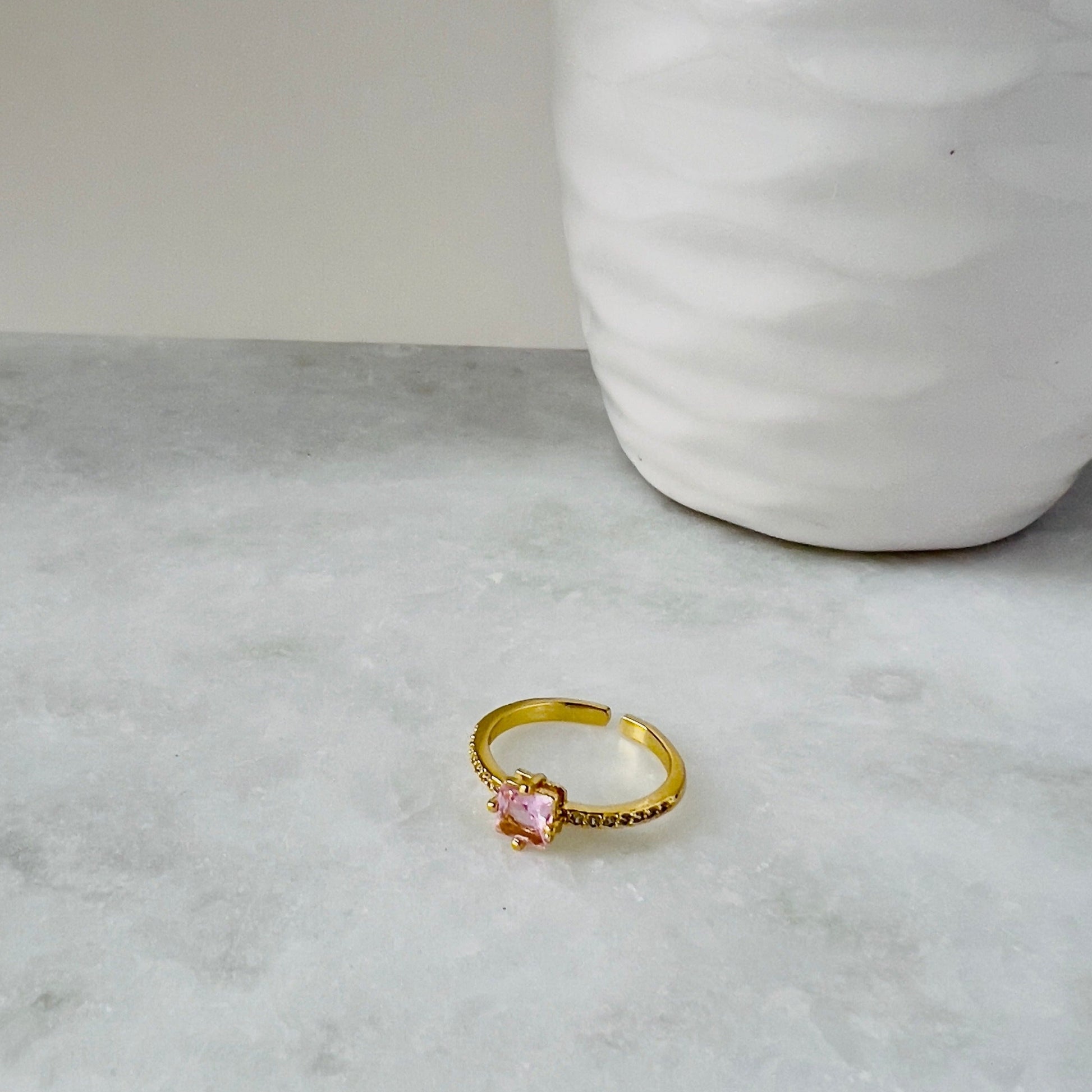 pink ring with squared rose pink crystal laying on a marble surface perfect to give away to a friend or as the perfect gift for an undergraduate