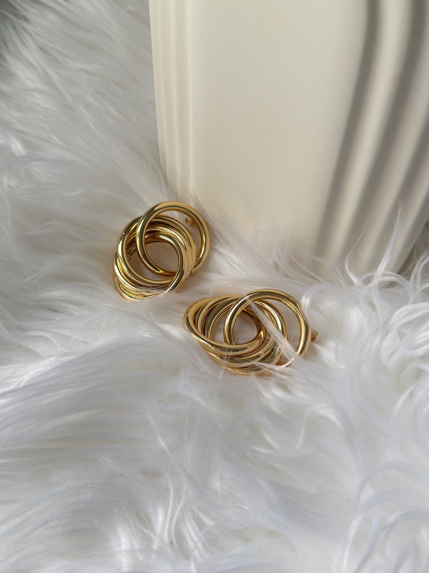 picture of intertwined earrings in gold plated in a bed of feathers