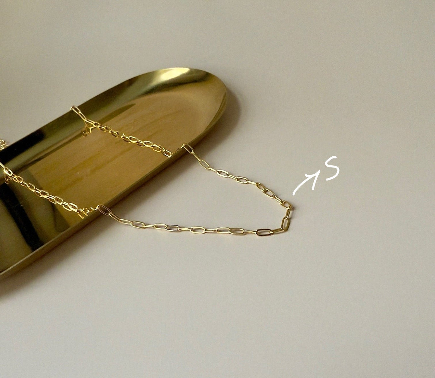 "Flat lay of a gold paperclip necklace placed on a marble surface, showcasing its trendy link design.