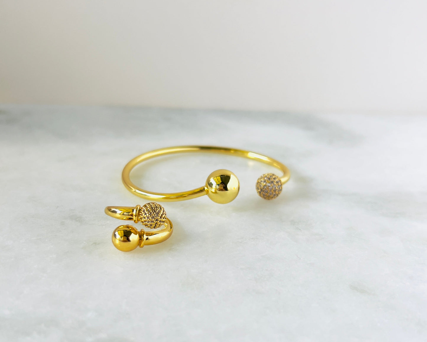 Luxurious gold-plated bangle with distinctive ball ends, one solid and one adorned with shimmering cubic zirconia stones. Perfect for those seeking a blend of classic elegance and modern sparkle
