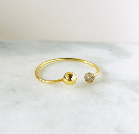Elegant gold-plated bangle featuring ball-shaped ends, with one solid gold ball and the other encrusted with sparkling cubic zirconia. This unique design adds a touch of sophistication and sparkle to any outfit."