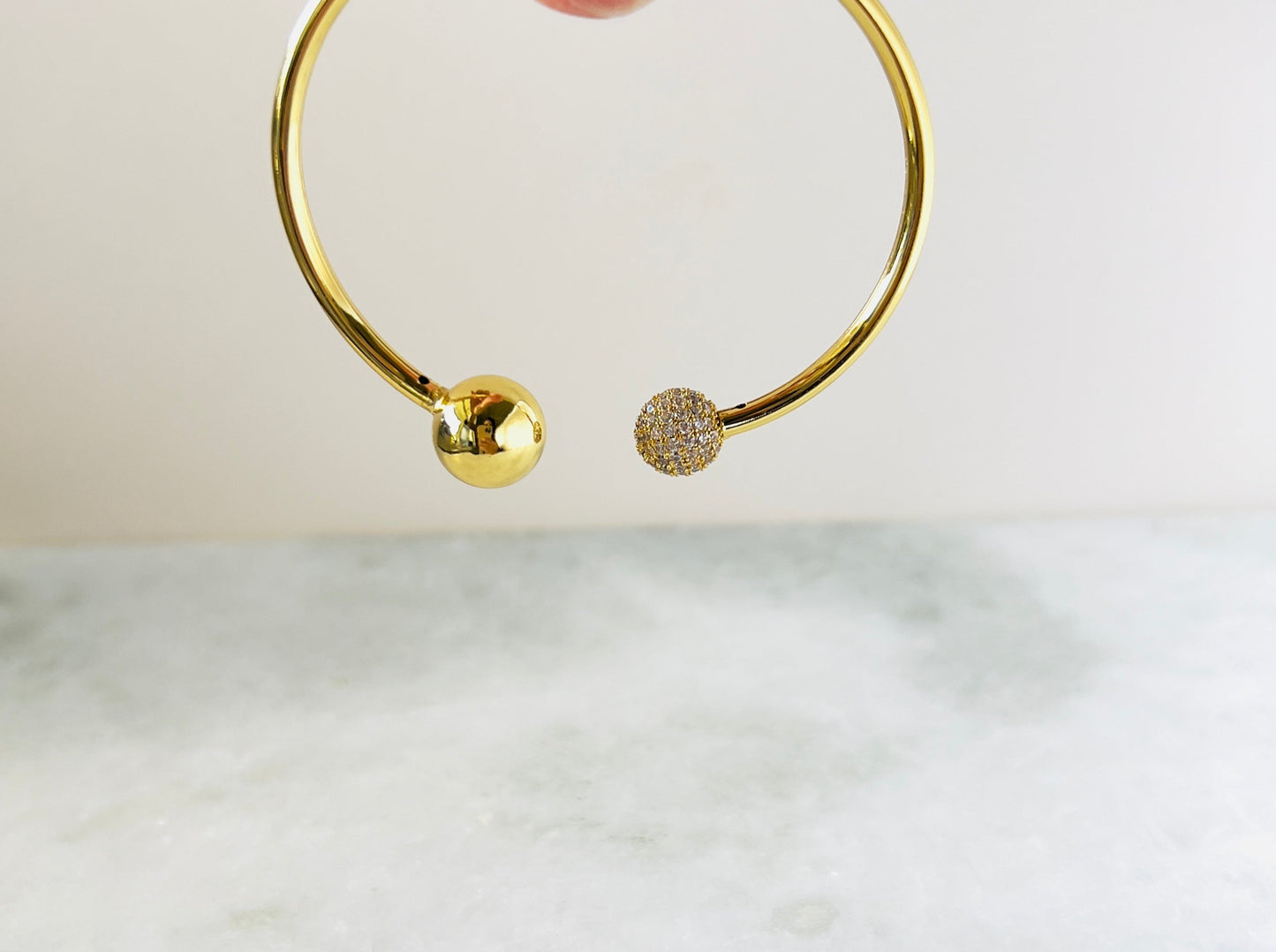Chic gold-plated bangle bracelet with contrasting ball ends, where one end is a solid gold ball and the other is covered in cubic zirconia. This stylish bangle offers a unique and glamorous accessory for any occasion
