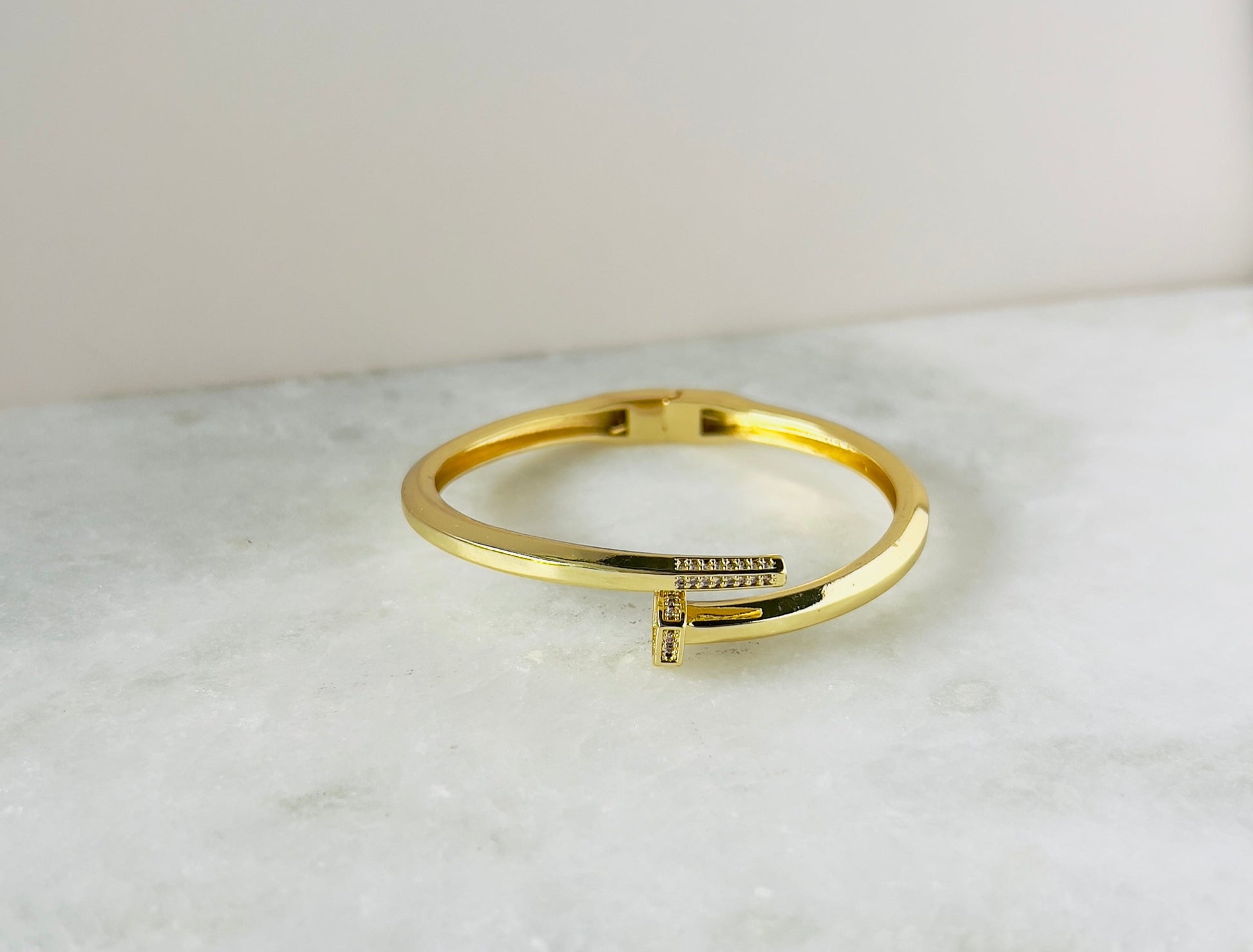 Elegant nail-shaped bangle adorned with sparkling zirconia stones, perfect for a stylish and modern accessory. This unique zirconia bangle adds a touch of sophistication to any outfit